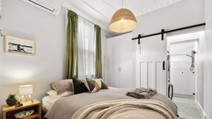 A bedroom with a bed, bedside table, lamp, and a view of a shower area. - Bondi Salt Soul - A Sepal Stay (Sydney)