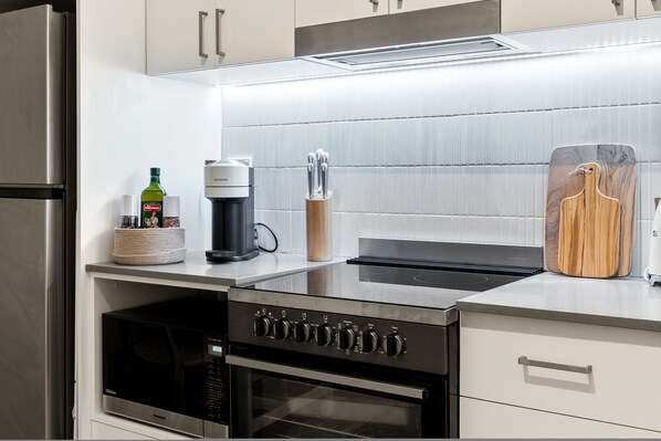 Et køkken med indbygget mikroovn, ovn og kaffemaskine på bordet.