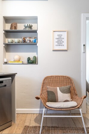 A wicker chair with cushions, a bookshelf with various items, and a framed sign on the wall. - Bondi Salt Soul - A Sepal Stay (Sydney)