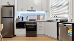 A modern kitchen with white cabinets, stainless steel appliances, and a window with blinds. - Bondi Salt Soul - A Sepal Stay (Sydney)