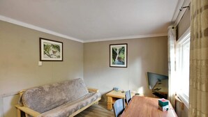 Una habitación con un sofá, una mesa de madera, dos sillas, un televisor y dos cuadros en la pared.