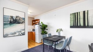 A dining area with a table and chairs, a kitchen in the background, and two large framed pictures on the walls. - Skynest Rivervale - Sepal Stay (Perth)