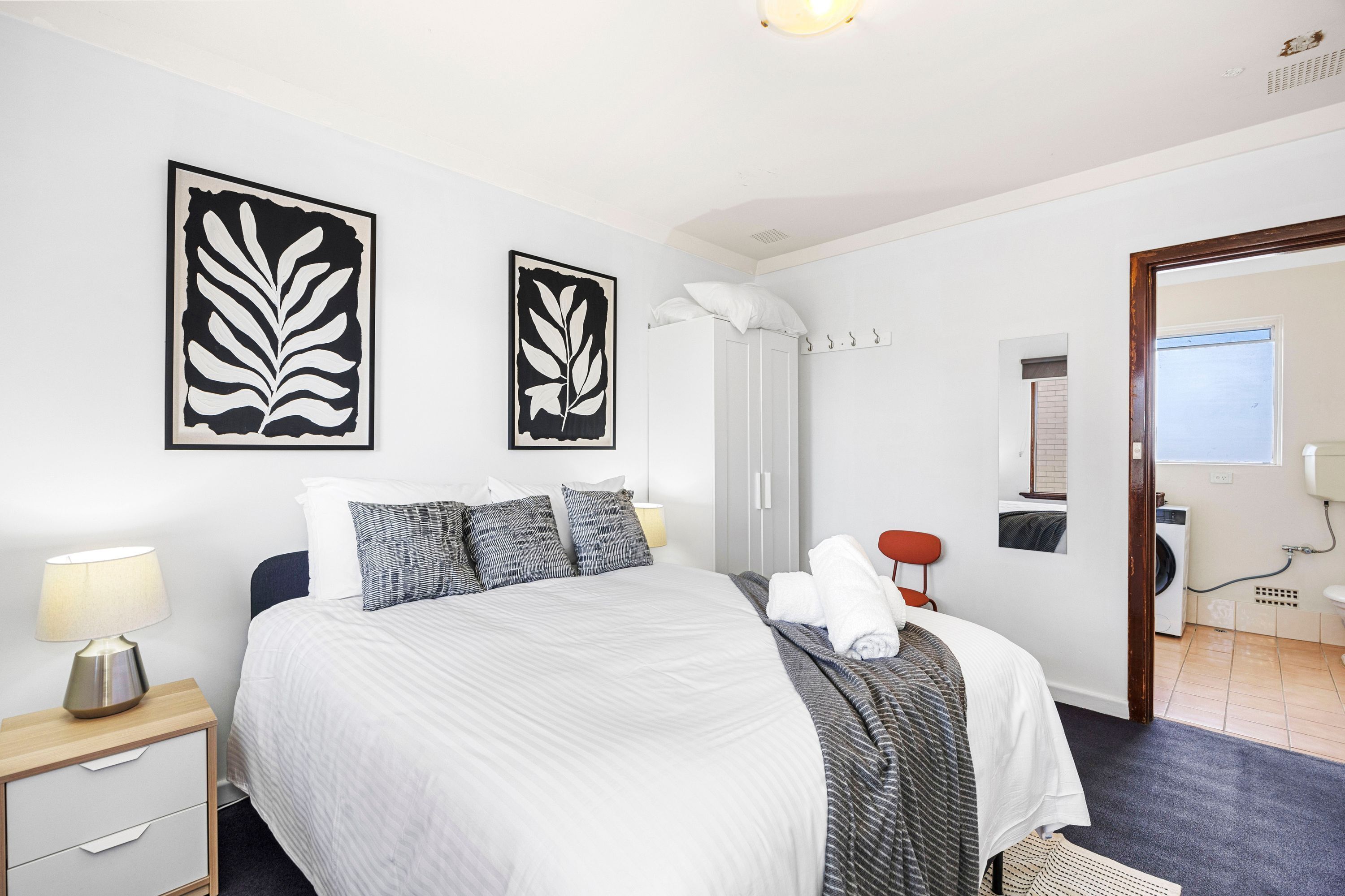 A neatly arranged hotel room with a bed, bedside table, lamp, artwork, and a view of the bathroom.