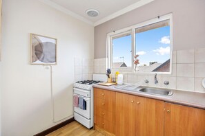 A kitchen with a stove, oven, sink, and window with a view of buildings. - Skynest Rivervale - Sepal Stay (Perth)