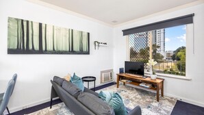 A living room with a sofa, a TV, a bookshelf, and a large painting on the wall. - Skynest Rivervale - Sepal Stay (Perth)