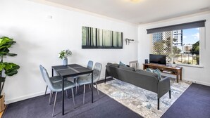Ein modernes Wohnzimmer mit Essbereich, einer Couch, einem Fernseher und einem großen Fenster.