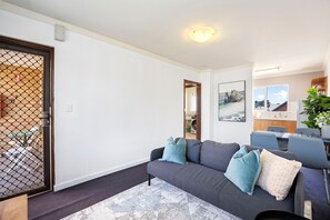 A living room with a grey sofa, a coffee table, and a dining area with chairs and a table. - Skynest Rivervale - Sepal Stay (Perth)
