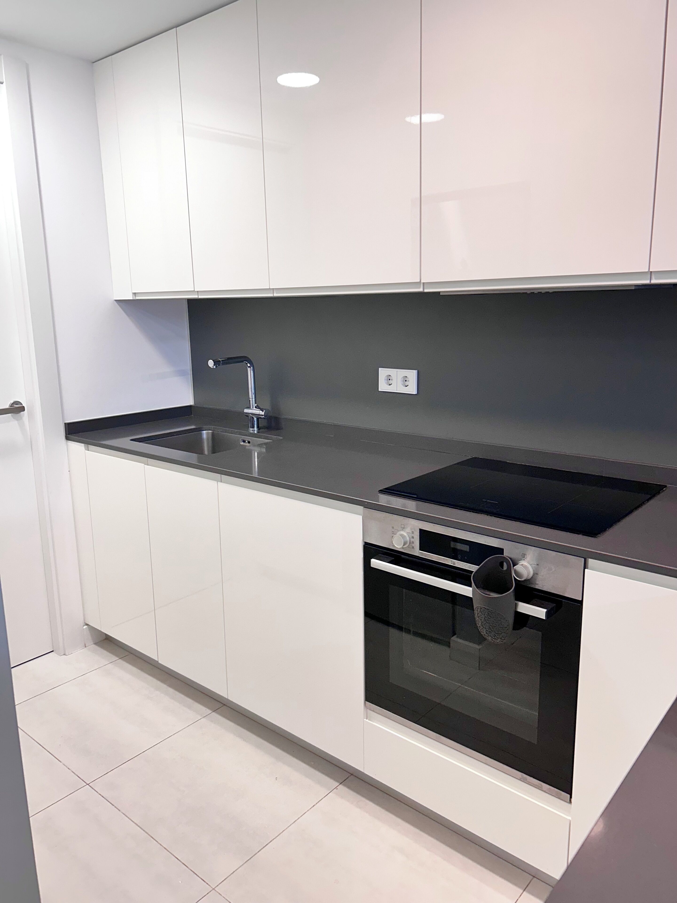 A modern kitchen with white cabinets, a stainless steel sink, and a built-in oven.