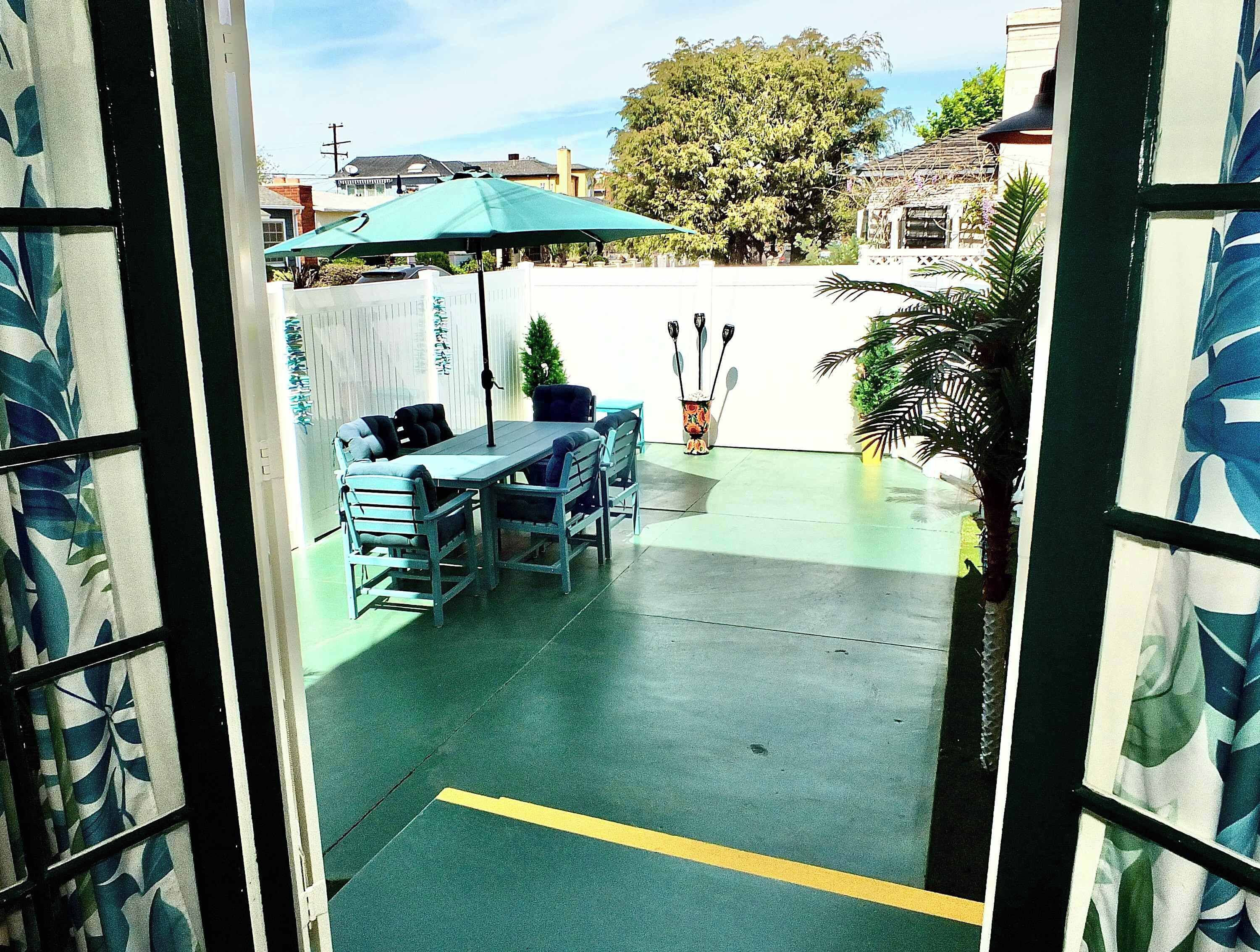 An outdoor patio with a table and chairs, a green umbrella, and a decorative plant.