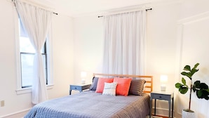 Une chambre à coucher avec un lit, des tables de chevet, une plante en pot et une fenêtre avec des rideaux.