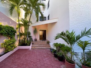 A modern building with a red-tiled courtyard, steps leading to a door, and various potted plants. - Casa 4 Estaciones (Puerto Morelos)