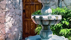 A stone fountain with multiple tiers in front of a wooden door and a stone wall. - Casa 4 Estaciones (Puerto Morelos)