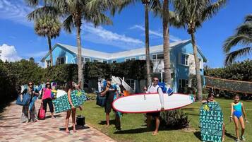 A group of people with surfboards in front of a blue house with palm trees.