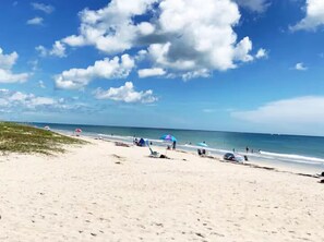 Uma praia com areia, alguns guarda-sóis e céu claro.