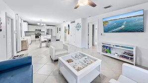 Un salon moderne avec un téléviseur, des meubles blancs et un ventilateur de plafond.