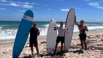 Four people holding surfboards on a beach with the ocean in the background.