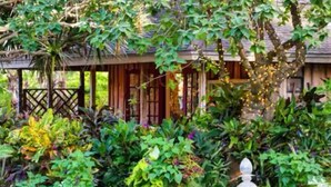 Une structure en bois dotée d’un porche abrité, entourée d’une végétation luxuriante et agrémentée d’une fontaine décorative.