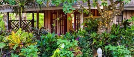 A wooden structure with a covered porch surrounded by lush greenery and a decorative fountain.