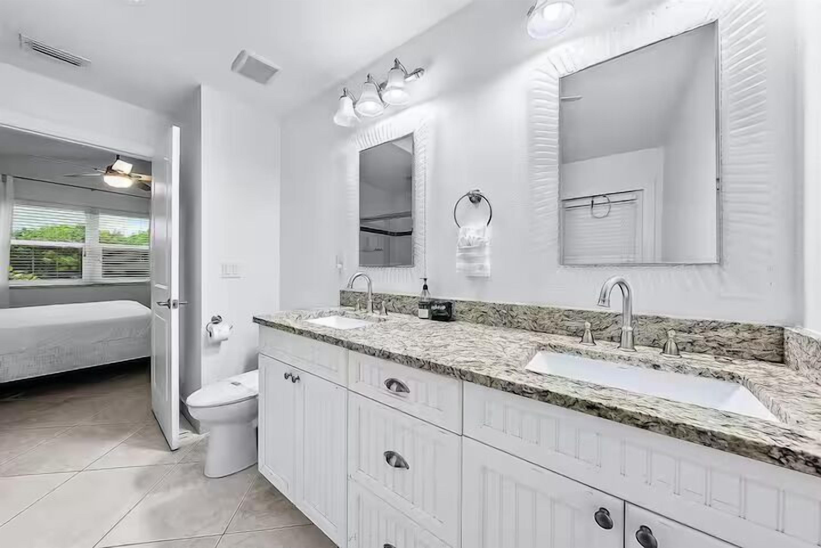 Une salle de bain avec deux lavabos, des toilettes, une douche et une fenêtre donnant sur un espace verdoyant.