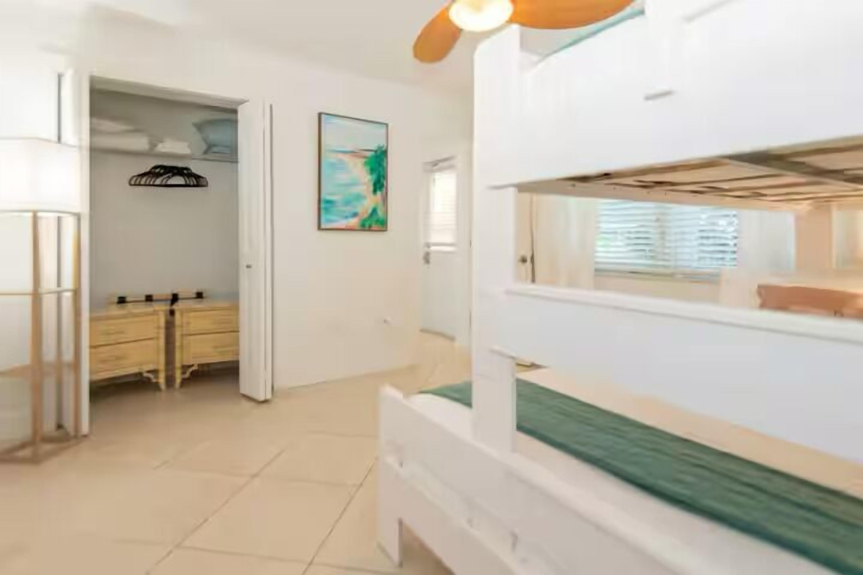 A bedroom with a bunk bed, a closet, a dresser, and a painting on the wall.
