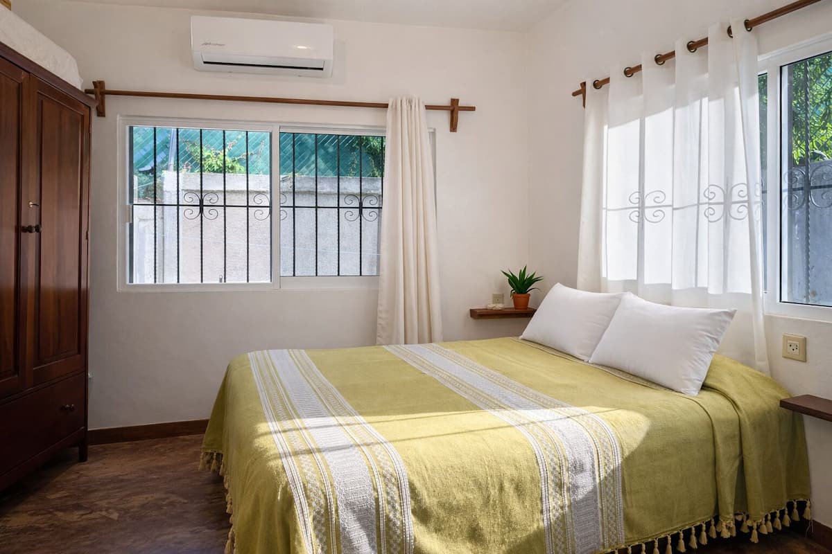 Un dormitorio con cama, ventana con cortinas, planta en maceta y armario de madera.