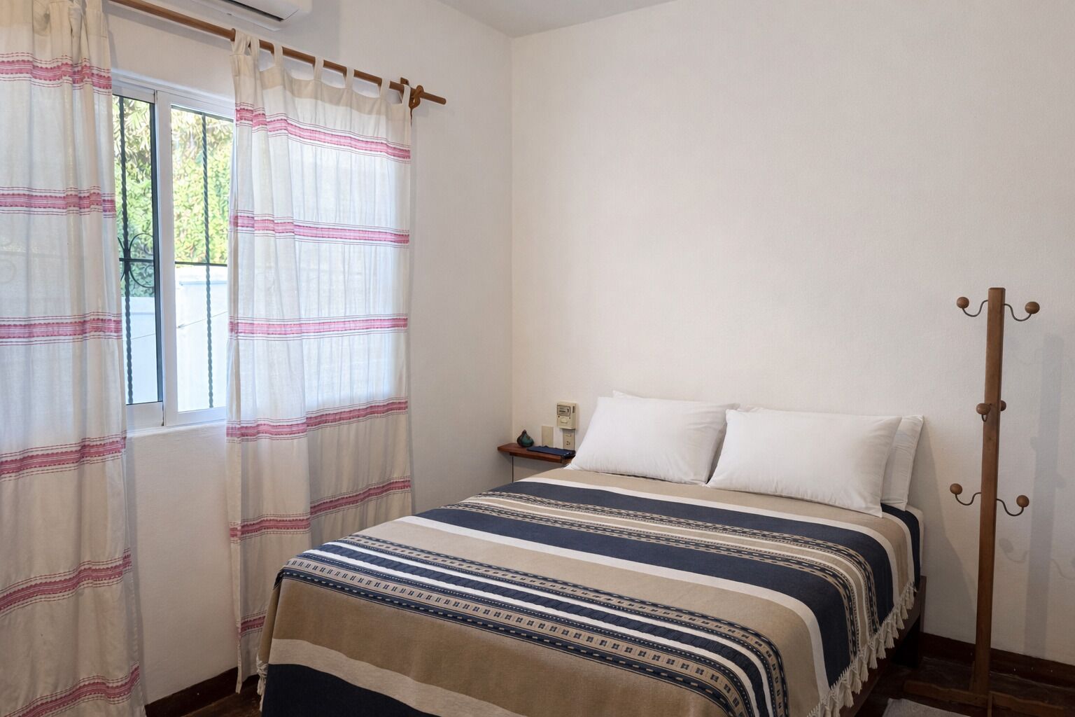Ein Schlafzimmer mit Bett, Nachttisch, Kleiderhaken und einem Fenster mit Vorhängen.