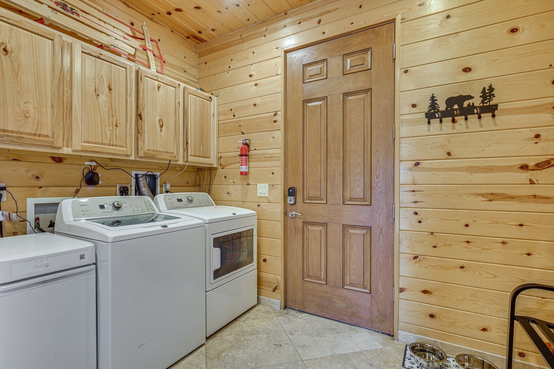 A wooden interior with a washing machine, dryer, and a door with a bear and trees decal.