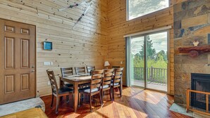 A wooden cabin interior with a dining table, chairs, a fireplace, and a large window. - Gorgeous 4-bedroom cabin in enjoyable Summerhaven getaway +game room (Summerhaven)