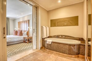 Ein Hotelzimmer mit einem großen Bett, einer separaten Sitzecke, einer Badewanne und einem Spiegel.