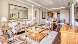 A spacious living room with a sofa, armchairs, a coffee table, and a dining area with chairs and a table. - Deluxe One-Bedroom Apartment (Sandton)