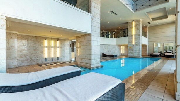 A modern indoor swimming pool with lounge areas, marble walls, and a high ceiling. - Deluxe One-Bedroom Apartment (Sandton)