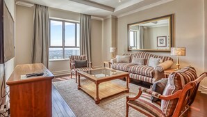 A spacious living room with a large window, a sofa, armchairs, a coffee table, and a TV. - Deluxe One-Bedroom Apartment (Sandton)
