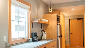 A compact kitchen with a window, a coffee maker, a refrigerator, and a wooden stool. - Studio 5 @ The Suites on Main (Leavenworth)