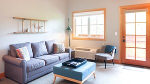 A living room with a sofa, a coffee table, a chair, a window, and a door. - Studio 5 @ The Suites on Main (Leavenworth)