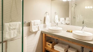 A modern bathroom with two sinks, a large mirror, and a glass shower enclosure. - Studio 5 @ The Suites on Main (Leavenworth)