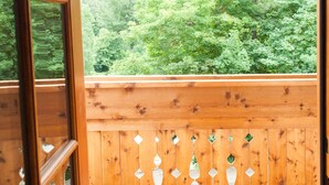 An open wooden balcony with a view of a forested hillside. - Studio 5 @ The Suites on Main (Leavenworth)