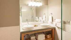 A modern bathroom with two sinks, a large mirror, and a shower area.