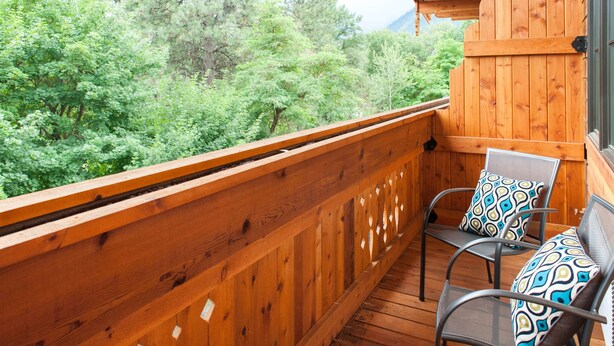 A wooden balcony with a view of dense green trees.