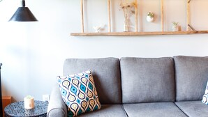 A grey sofa with patterned cushions, a wooden shelf with decorative items, and a black floor lamp.