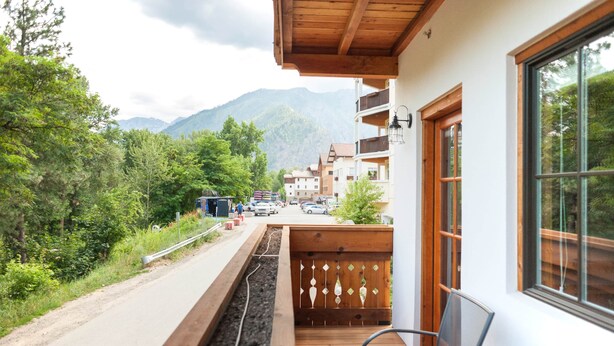 A balcony with a view of a road and mountains, a chair, and a wooden railing. - Studio 2 @ The Suites on Main (Leavenworth)