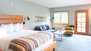 A bedroom with a bed, a sofa, a small table, and a door. - Studio 2 @ The Suites on Main (Leavenworth)