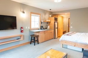 A compact room with a kitchenette, a bed, a TV, and a fire extinguisher. - Studio 2 @ The Suites on Main (Leavenworth)