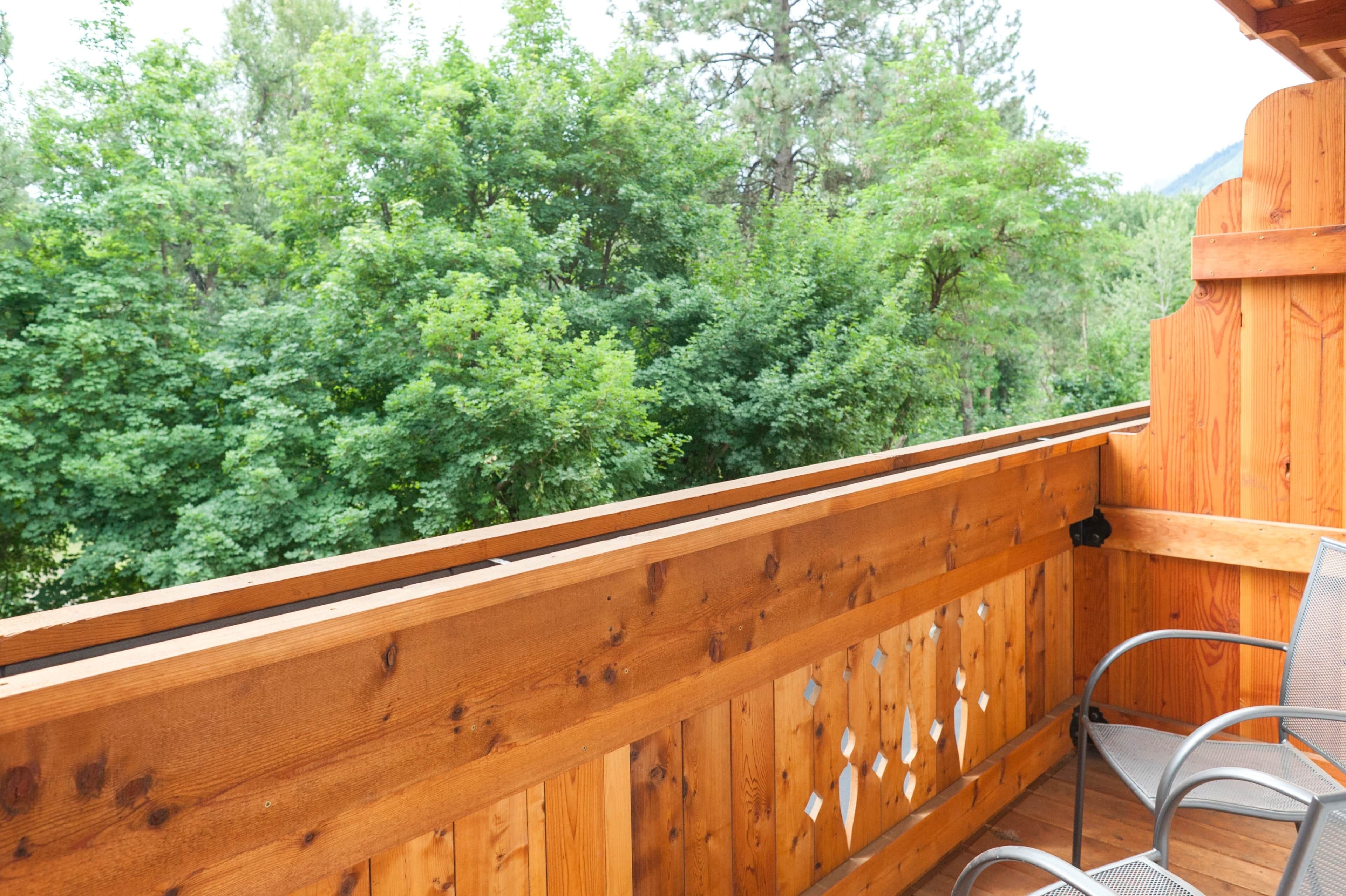 Un balcon en bois avec une chaise en métal, donnant sur une forêt dense.