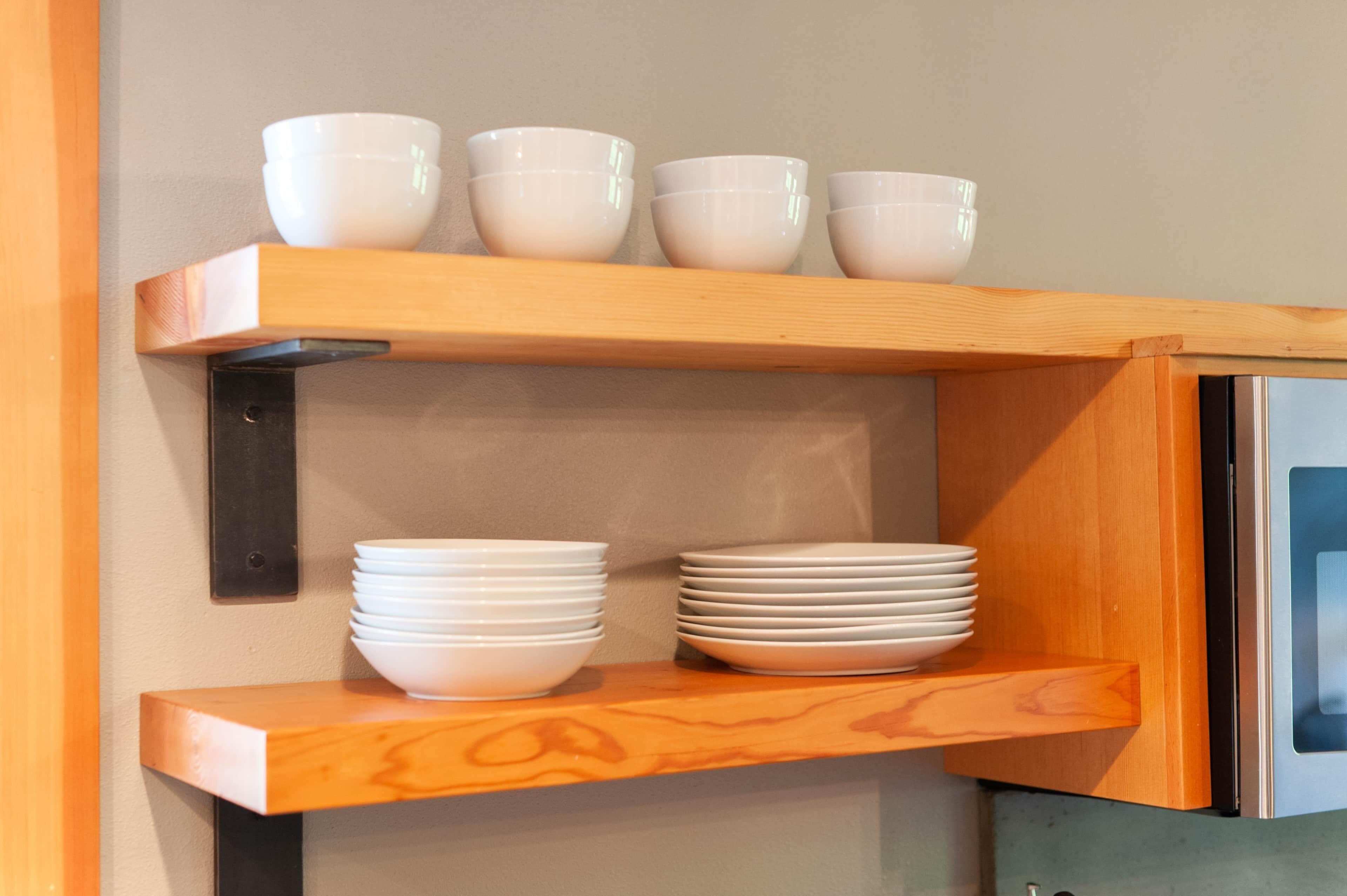 A kitchen with wooden shelves holding white bowls and plates.
