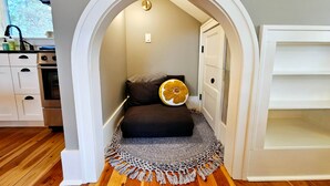 A cozy room with a small bed, a decorative rug, and a kitchen visible through an archway. - The Alley House (Leavenworth)