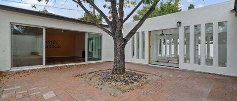Un árbol en un patio con suelo de ladrillo, rodeado por un edificio con ventanas grandes y una puerta con la leyenda 'enix STICE'.