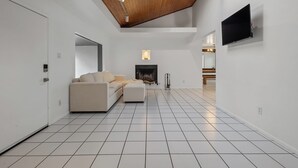 Ein modernes Wohnzimmer mit Kamin, einer Couch, einem an der Wand montierten Fernseher und einem Oberlicht.