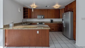 Una cocina con armarios de madera, un refrigerador de acero inoxidable, un microondas y una encimera de granito.