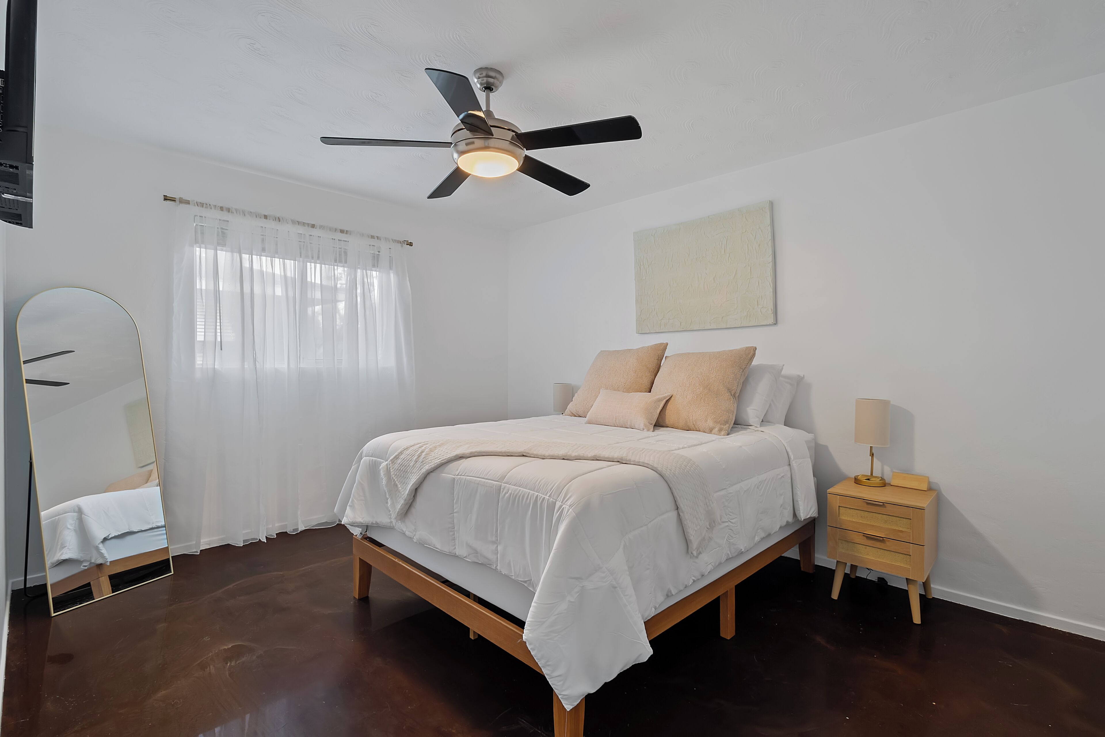 A bedroom with a bed, a nightstand, a ceiling fan, a window with curtains, and a mirror.