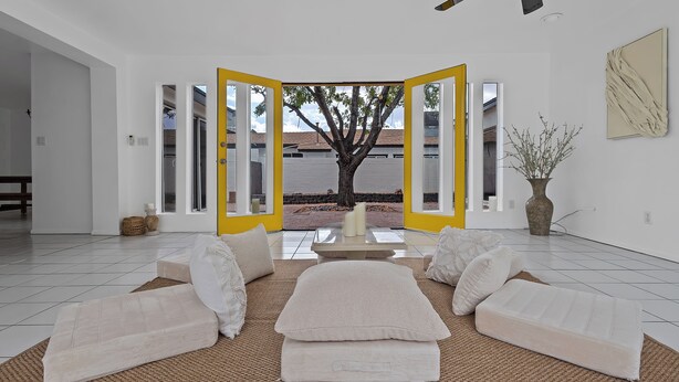 Una sala de estar con un ventanal grande, un árbol fuera y un conjunto de sofás.